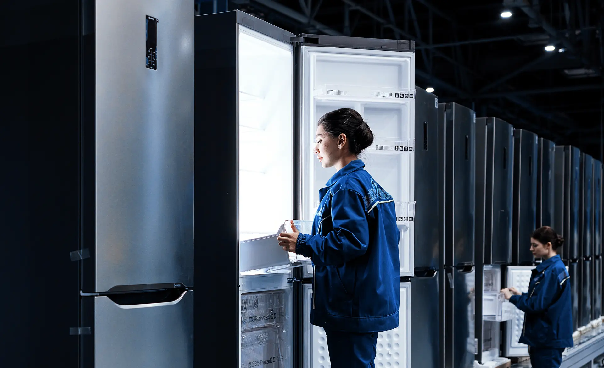 Electronics manufacturing facility worker inspecting refrigerators on a production line.